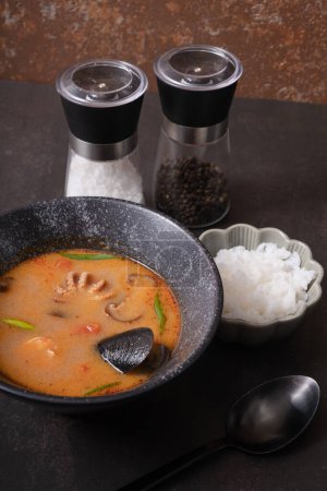 Tom yum soup with seafood and rice on dark background angle view.