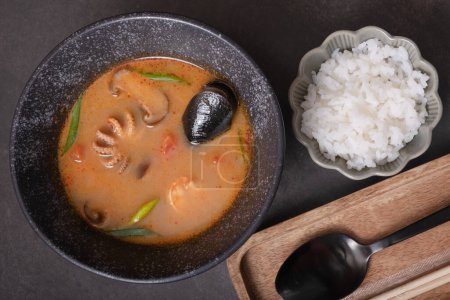 Tom yum soup with seafood and rice ondark background top view.