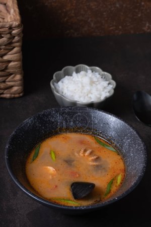 Tom yum soup with seafood and rice on dark background angle view.