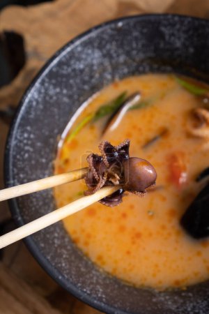 Close up octopus in chopsticks on the background of tom yum soup.