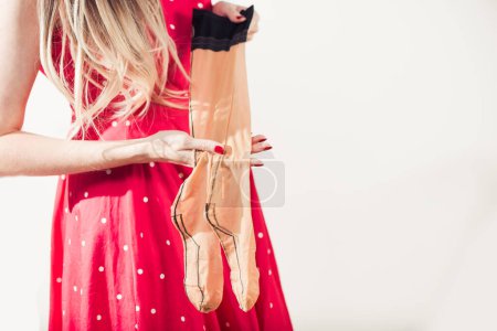 Photo for Young woman in red dott dress holding tan vintage stockings in hands - Royalty Free Image