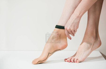Photo for Youg wooman in red dress dressing up sexy vintage tan  stockings on her feet - Royalty Free Image
