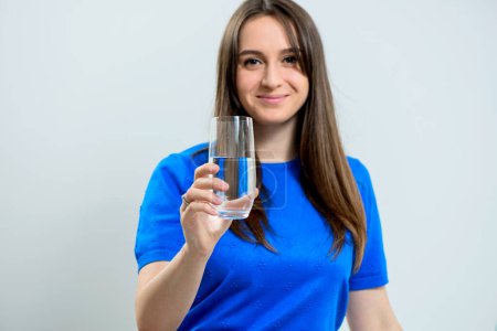Téléchargez les photos : Jeune femme souriante en robe bleue tenant un verre d'eau cristalline prêt à boire - en image libre de droit
