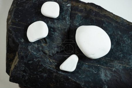 Téléchargez les photos : Quatre pierres blanches lisses posées sur une surface de pierre plate noire - en image libre de droit
