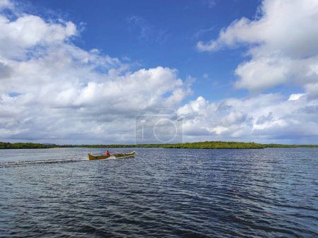 Foto de Un hombre pilota un bote motorizado en medio de un paisaje surrealista de nubes y manglares. - Imagen libre de derechos