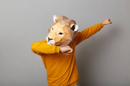 Indoor shot of anonymous man wearing lion mask and orange sweatshirt isolated over gray background, making dabbing movement, famous internet meme of success victory.