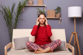 Photo of sick unhealthy Caucasian female dressed in home clothes sitting on cough in her apartment, suffering headache, having flu symptoms, massaging her temples, has migraine. Mouse Pad 620920364
