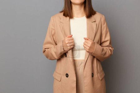 Photo for Horizontal shot of self-confident unknown faceless woman wearing beige official style costume standing isolated over gray background, holding her jacket. - Royalty Free Image