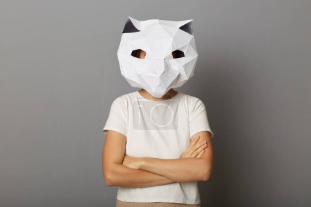 Foto de Indoor shot de mujer orgullosa confiada usando máscara de papel de gato y camiseta blanca posando aislada sobre fondo gris, de pie con las manos dobladas, expresando confianza. - Imagen libre de derechos