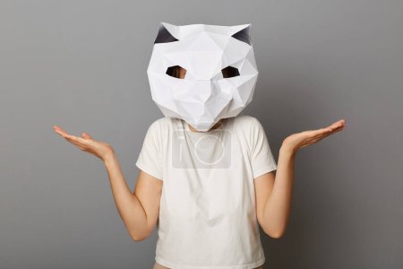 Photo for Portrait of uncertain helpless unknown woman wearing cat paper mask and white T-shirt posing isolated over gray background, shrugging shoulders, spread hands, doesn't know answer. - Royalty Free Image