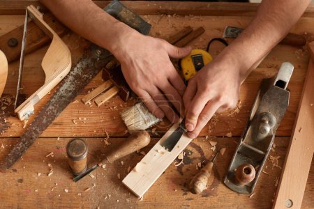 Téléchargez les photos : Top view of man hand using chisel on wooden table, working among the shavings and set of carpentry tools, profession, hobby, carpentry, woodwork, wood carving. - en image libre de droit