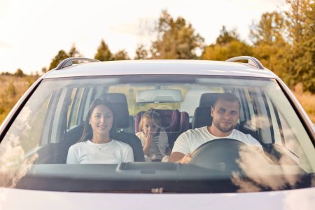 Foto de Retrato de la familia conduciendo el fin de semana, mamá y papá con su hija sentada en el coche, teniendo vacaciones, disfrutando pasar tiempo juntos, sonriendo felizmente. - Imagen libre de derechos
