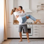 Attractive family man and woman having fun in kitchen celebrating relocating guy holding his girlfriend or wife and kissing expressing romantic feelings