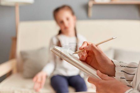 Weibliches Kind bei einer Sitzung mit einem Psychologen, der Notizen über ihren emotionalen und geistigen Zustand macht und sorgfältig auf die Sorgen und Probleme des Mädchens hört.
