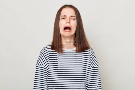 Photo for Unhappy sad brown haired woman wearing striped shirt posing isolated over gray background crying feeling despair hearing very bad news. - Royalty Free Image