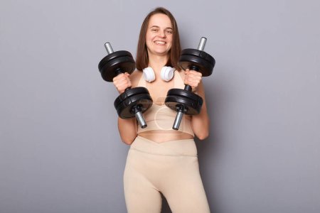 Photo for Pretty athletic woman wearing top holding red barbells in hands isolated on gray background doing sport workout healthy lifestyle body care. - Royalty Free Image