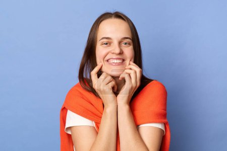 Photo for Optimistic smiling woman wearing white t-shirt and jumper over neck standing isolated over blue background being in good mood being extremely happy. - Royalty Free Image