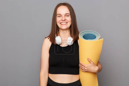 Photo for Fitness workout routine. Yoga and relaxation. Athletic body strength. Smiling woman holding rolled fitness mat dressed in activewear isolated over gray background. - Royalty Free Image