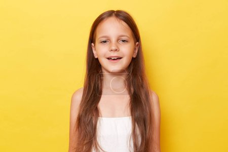 Photo for Positive optimistic little girl with long hair standing isolated over yellow background looking at camera with happy face expressing happiness being in good mood. - Royalty Free Image