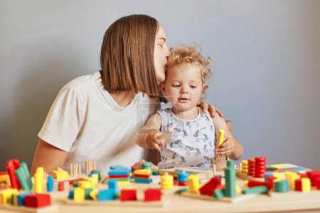 Family bonding and cheerful upbringing. Playful games and imaginative learning. Mother and daughter playing learning games with wooden toys mom kissing kid.