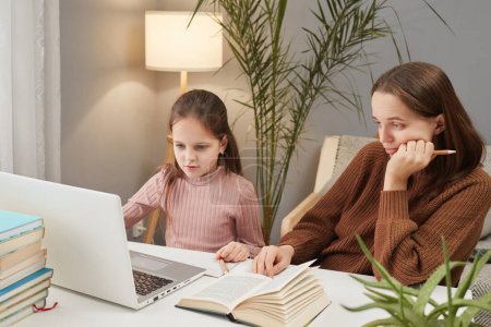 Apprentissage à domicile avec des ordinateurs. Aide parentale dans les études informatiques de l'enfant. ennuyé mère et fille en utilisant ordinateur portable à la maison intérieur regarder leçon en ligne femme aider à son enfant
