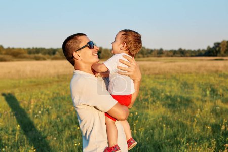 Young father and his infant daughter enjoying happy time and hot sunny days together in summer green meadow daddy embracing charming baby girl