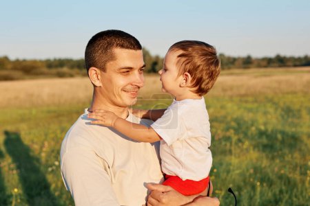 Happy father's day. Father and baby daughter smiling in meadow child hugging daddy with green grass on background having fun outdoor during hot summer days