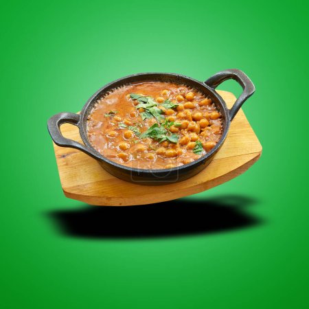 Floating chana masala in little pan on green gradient background