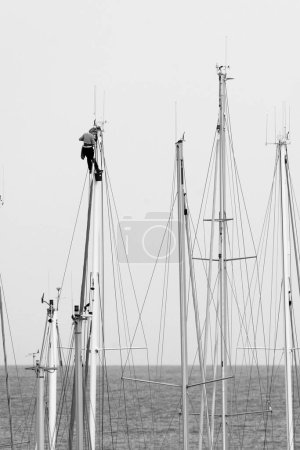 Foto de Italia, Sicilia, Mar Mediterráneo, Marina di Ragusa (Provincia de Ragusa); mujer subiendo a un mástil de velero en catamarán en el puerto - Imagen libre de derechos