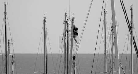 Foto de Italia, Sicilia, Mar Mediterráneo, Marina di Ragusa, hombre trabajando en un mástil de velero en el puerto - Imagen libre de derechos