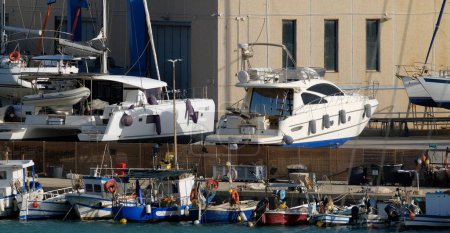 Foto de Italia, Sicilia, Marina di Ragusa (provincia de Ragusa), 28 de abril de 2024, barcos de pesca locales y yates de lujo en tierra en el puerto - EDITORIAL - Imagen libre de derechos