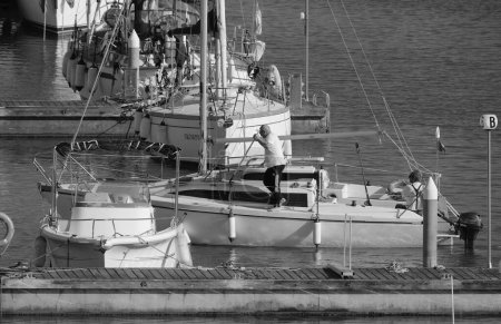 Foto de Italia, Sicilia, Mar Mediterráneo, Marina di Ragusa (Provincia de Ragusa); 12 de mayo de 2024, hombres en un velero y yates de lujo en el puerto - EDITORIAL - Imagen libre de derechos