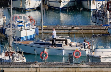 Foto de Italia, Sicilia, Mar Mediterráneo, Marina di Ragusa (Provincia de Ragusa); 12 de mayo de 2024, hombres en un velero y yates de lujo en el puerto - EDITORIAL - Imagen libre de derechos