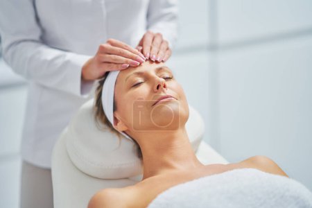 Téléchargez les photos : Jeune femme agréable ayant massage du visage dans le spa. Photo de haute qualité - en image libre de droit