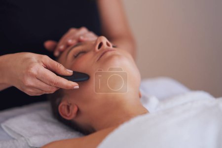 Téléchargez les photos : Brunette femme ayant un massage en pierre sur le visage. Photo de haute qualité - en image libre de droit