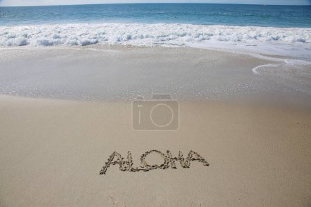 Foto de Aloha written in the sand on the beach.  message handwritten on a smooth sand beach - Imagen libre de derechos