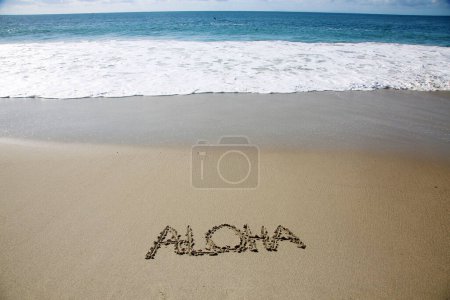 Téléchargez les photos : Aloha  written in the sand on the beach.  message handwritten on a smooth sand beach - en image libre de droit