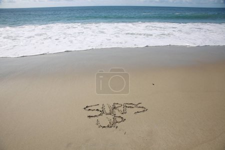 Foto de Surfs up written in the sand on the beach.  message handwritten on a smooth sand beach - Imagen libre de derechos