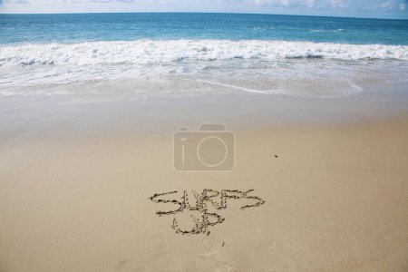 Foto de Surfs up written in the sand on the beach.  message handwritten on a smooth sand beach - Imagen libre de derechos