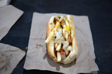 Foto de Hot Dog. A grilled World Famous Original Hot Dog is topped with French Fries, world famous Chili sauce, a slice of American cheese, French's mustard and grilled onions - Imagen libre de derechos