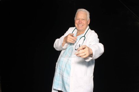 Foto de Médico. Un médico amable y amable sonríe sobre un fondo negro. Médico masculino caucásico sonriente con uniforme médico blanco y estetoscopio. Amistoso Doctor. - Imagen libre de derechos