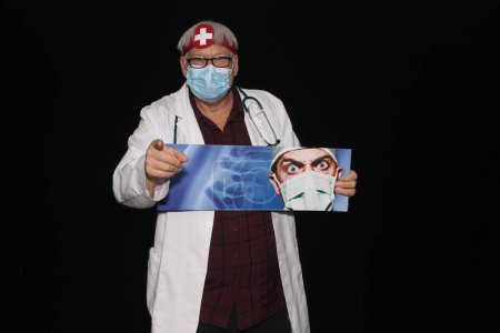 Téléchargez les photos : Médical. Un médecin amical et aimable sourit en se tenant debout avec une affiche avec son portrait sur elle avec un fond noir. Médecin homme caucasien souriant portant un uniforme médical blanc et stéthoscope - en image libre de droit