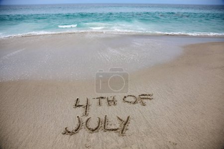 Foto de 4th of july written in the sand on the beach.  message handwritten on a smooth sand beach - Imagen libre de derechos