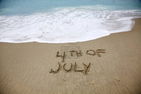 Foto de 4th of july written in the sand on the beach.  message handwritten on a smooth sand beach - Imagen libre de derechos