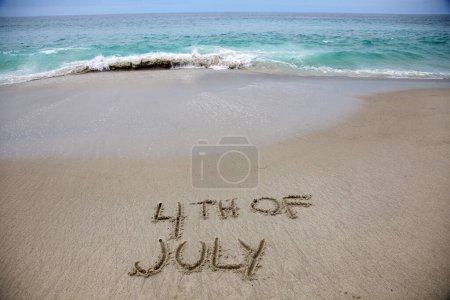 Téléchargez les photos : 4th of july written in the sand on the beach.  message handwritten on a smooth sand beach - en image libre de droit