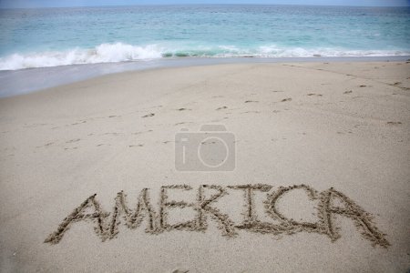Foto de America written in the sand on the beach.  message handwritten on a smooth sand beach - Imagen libre de derechos
