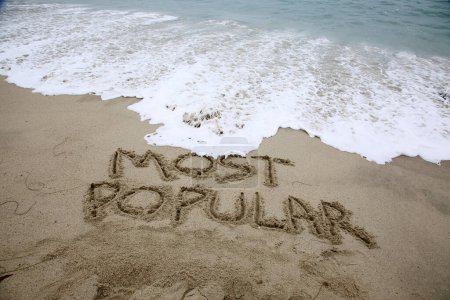 Foto de Most popular written in the sand on the beach.  message handwritten on a smooth sand beach - Imagen libre de derechos