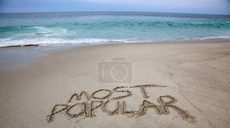 Téléchargez les photos : Most popular  written in the sand on the beach.  message handwritten on a smooth sand beach - en image libre de droit