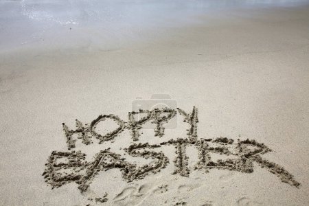 Foto de Semana Santa Hoppy. Las palabras HOPPY EASTER escritas en la arena junto al océano. - Imagen libre de derechos