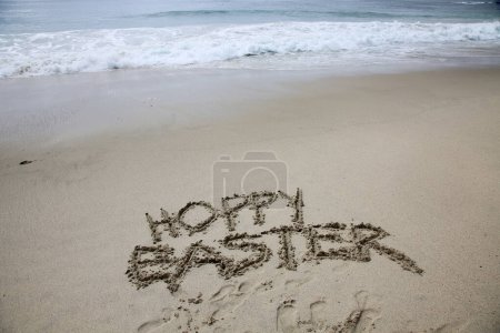 Foto de Hoppy Easter. The words HOPPY EASTER written in the sand by the ocean. - Imagen libre de derechos